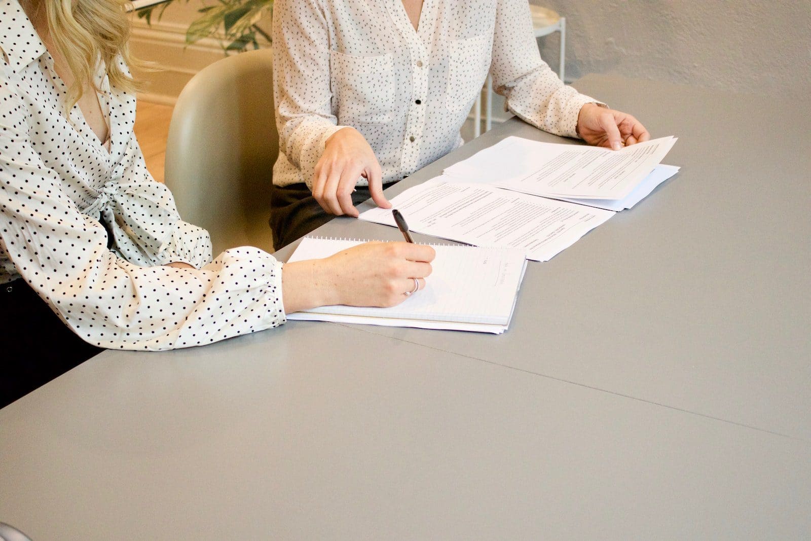 Frau unterschreibt auf weißem Druckerpapier neben einer Frau, die kurz davor steht, die Dokumente zu berühren
